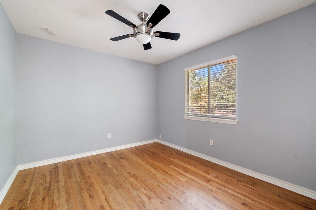 Empty room with hardwood floors, gray walls, a ceiling fan, and a window with blinds.