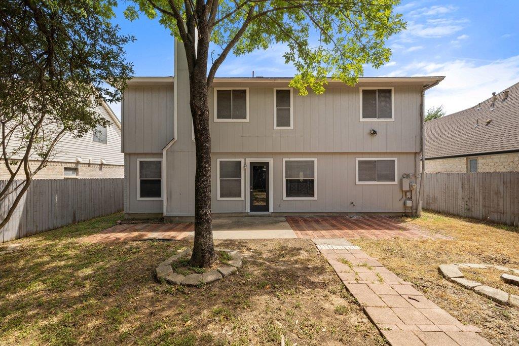 Two-story beige home viewed from the backyard, with a large shade tree and paved walkway.