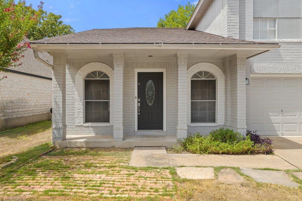 Light brick home with a covered porch, arched windows, and a dark front door.