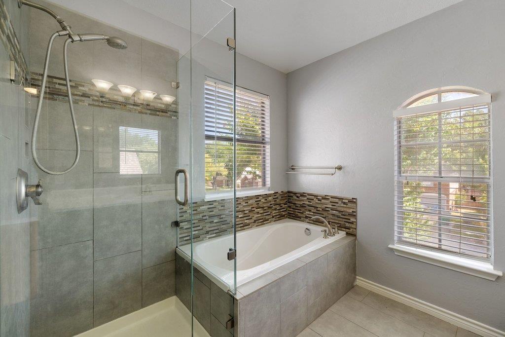 Bathroom with a glass-enclosed shower, built-in soaking tub, and two windows with white blinds.