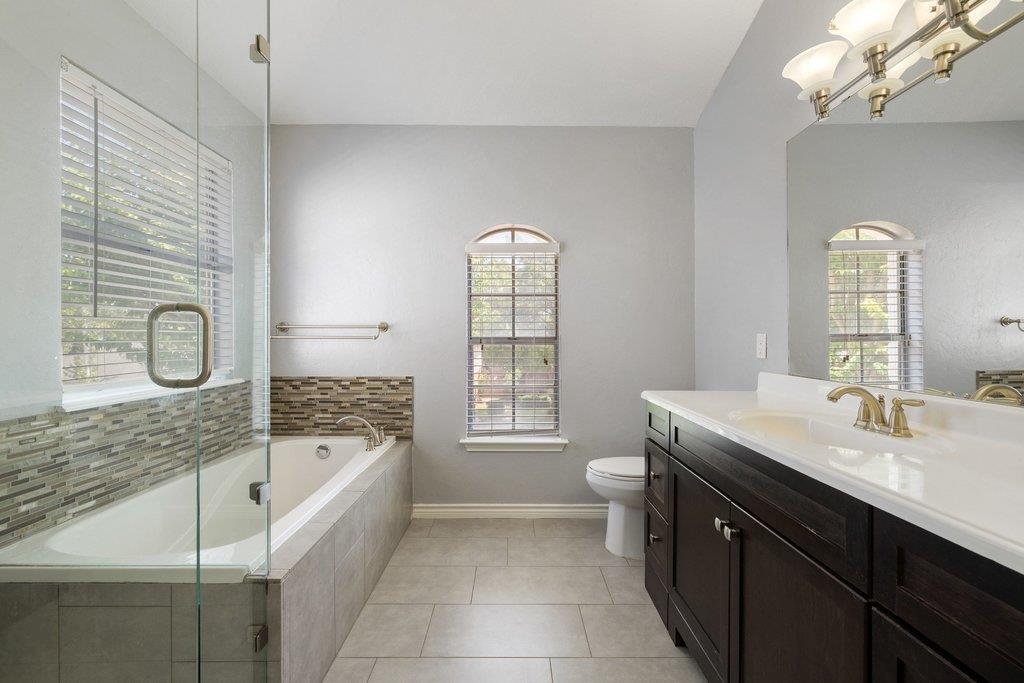 Bathroom with a glass-panel bathtub, dark wood vanity, tiled floor, and arched windows.