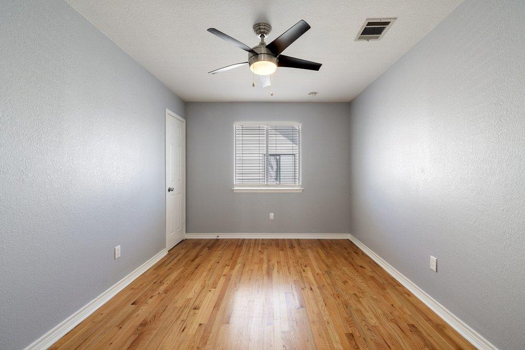 Empty bedroom with hardwood floors, gray walls, and a ceiling fan.