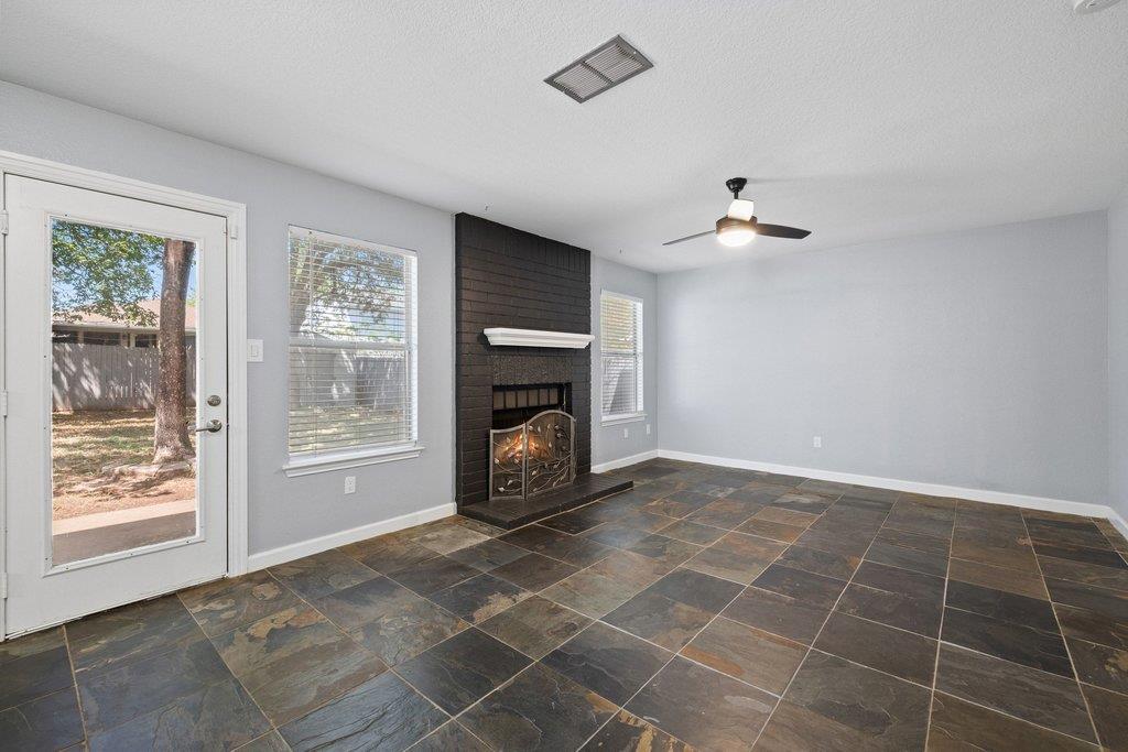 Empty living room with dark slate tile, a black brick fireplace, and a glass exterior door.
