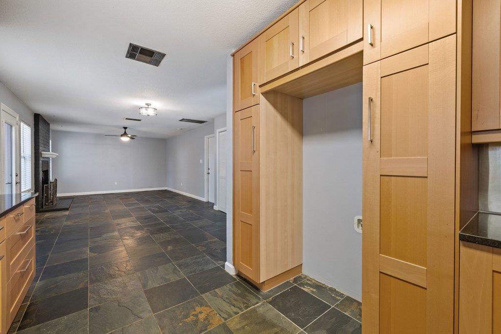 Kitchen and adjoining living area with honey-colored cabinets, slate tile, and a fireplace.