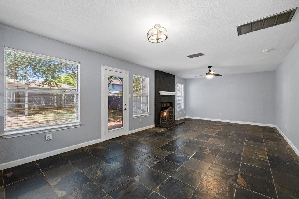 Vacant living room with slate tile floors, large windows, and a black brick fireplace.