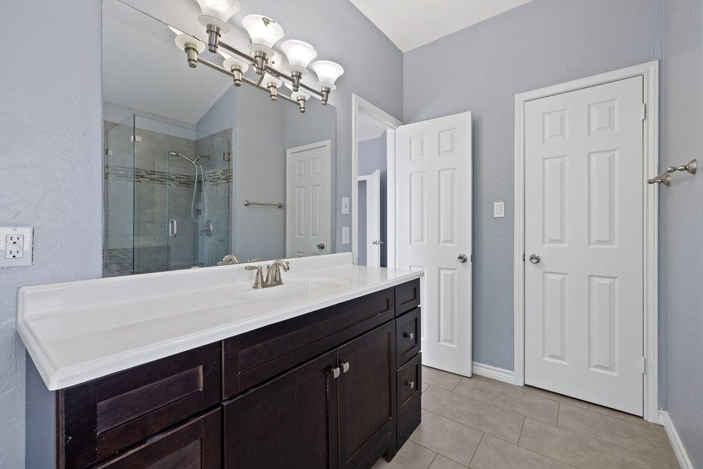 Bathroom with a dark wood vanity, long white countertop, large mirror, and glass-enclosed shower.