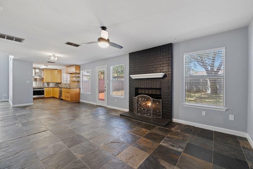 Living room with a dark brick fireplace, slate tile floors, and an open kitchen.