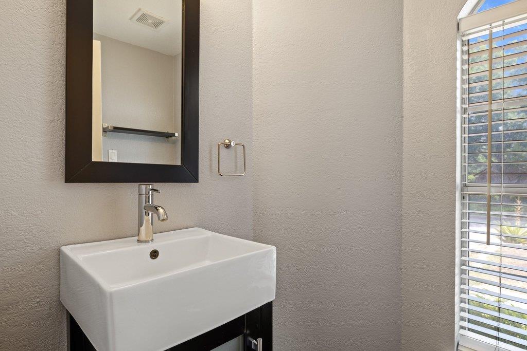 Bathroom sink with a dark-framed mirror and a tall window with blinds.