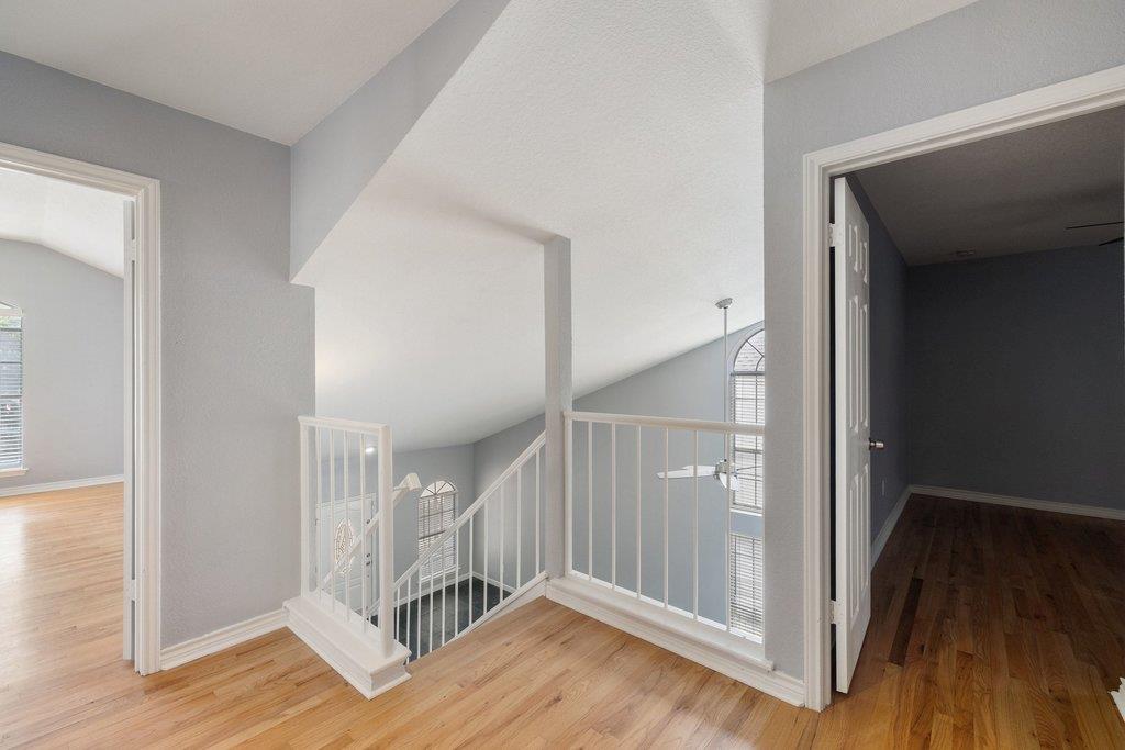 Upstairs landing with an open staircase, white railings, light wood floors, and tall arched windows.