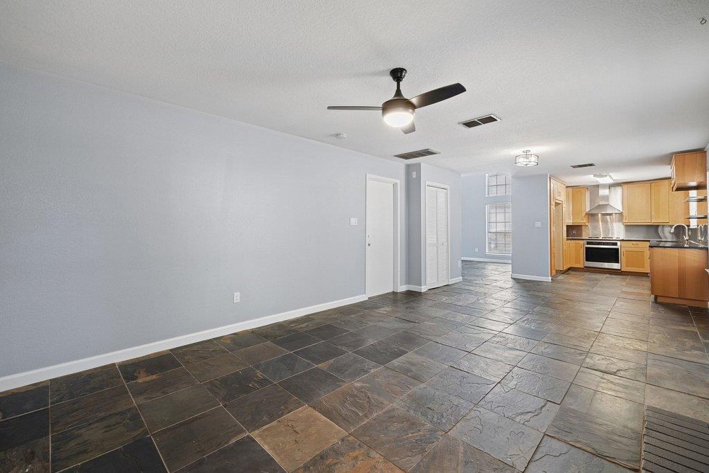 Open tiled living area leading into a kitchen with wood cabinets and stainless steel appliances.