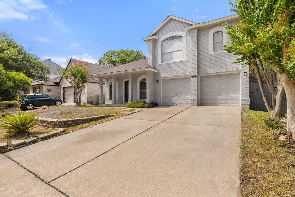 Two-story gray brick home with a double garage and broad concrete driveway.