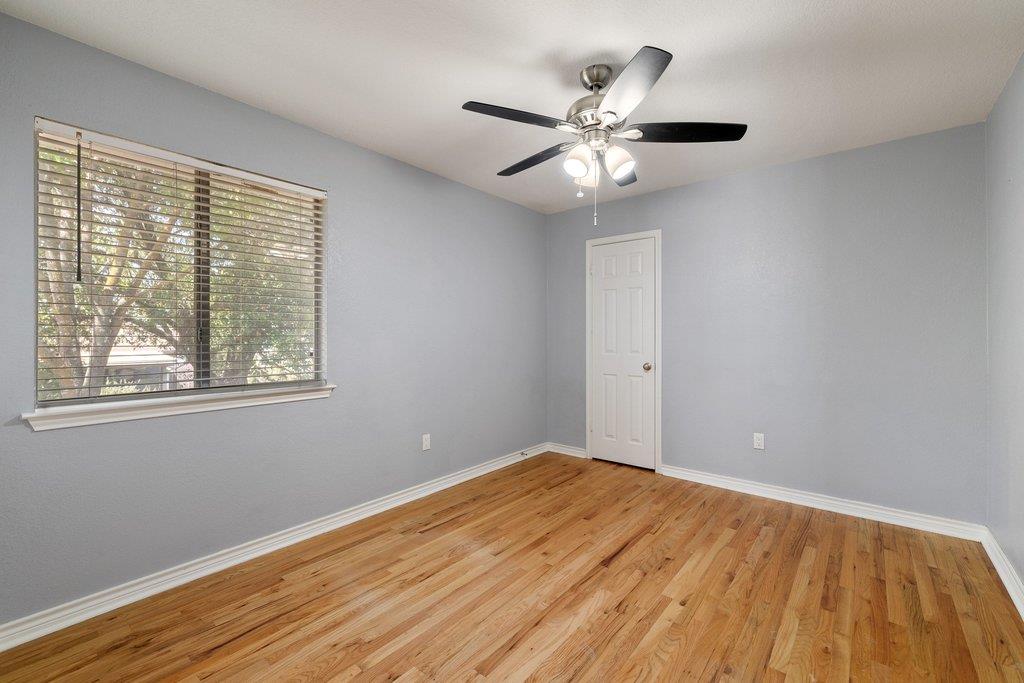 Empty bedroom with hardwood floors, a ceiling fan, and a wide window with blinds.
