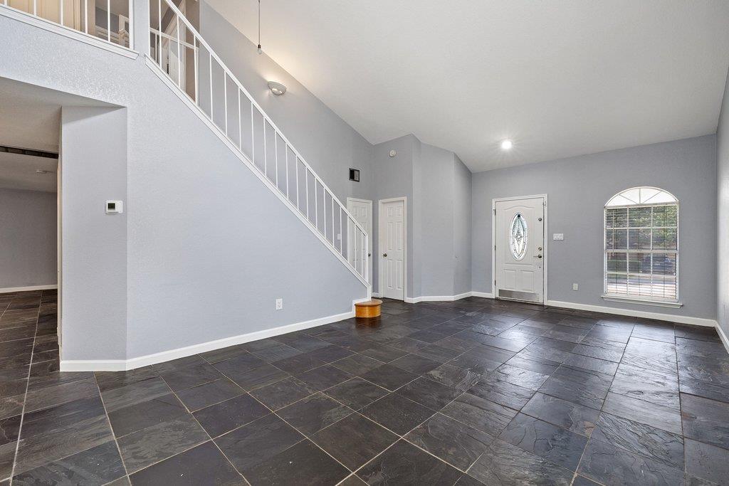 Empty home entry with slate-look tile, a white staircase, and an arched window beside the front door.