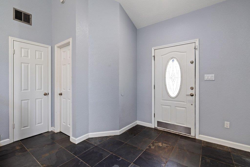 Empty entryway with dark tile floors and a white front door with an oval glass window.