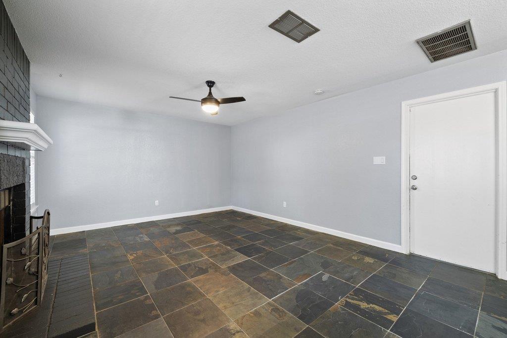 Empty room with multicolored tile flooring, a ceiling fan, and a brick fireplace.