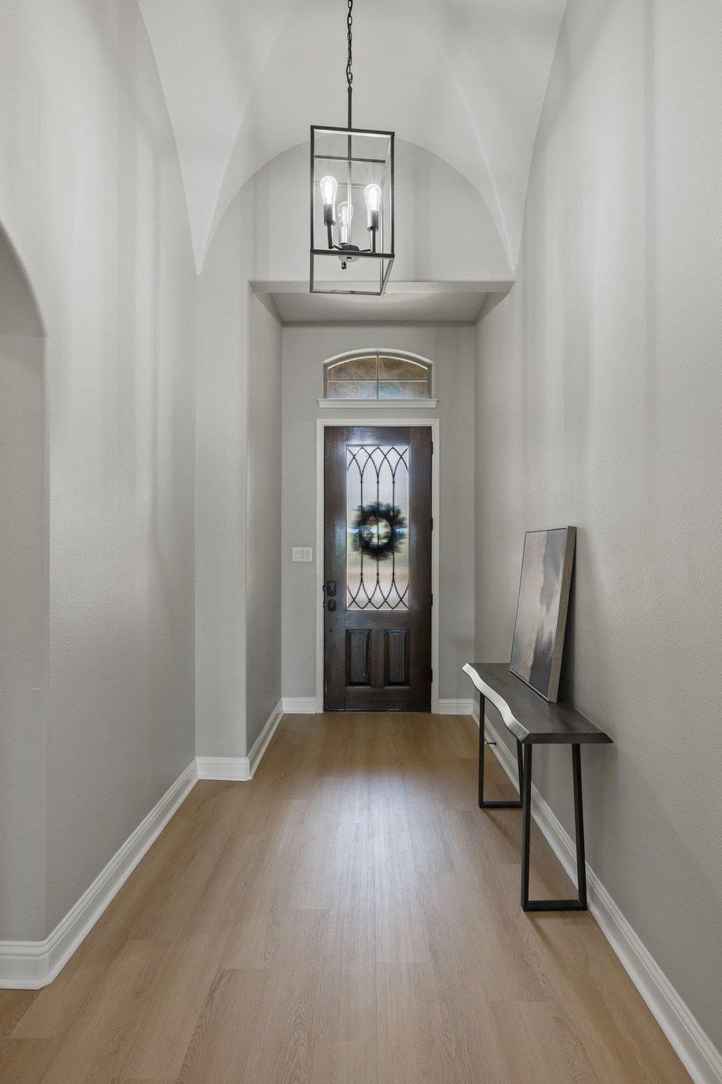 Entry foyer with vaulted ceiling, dark glass-paneled front door, and geometric pendant light.