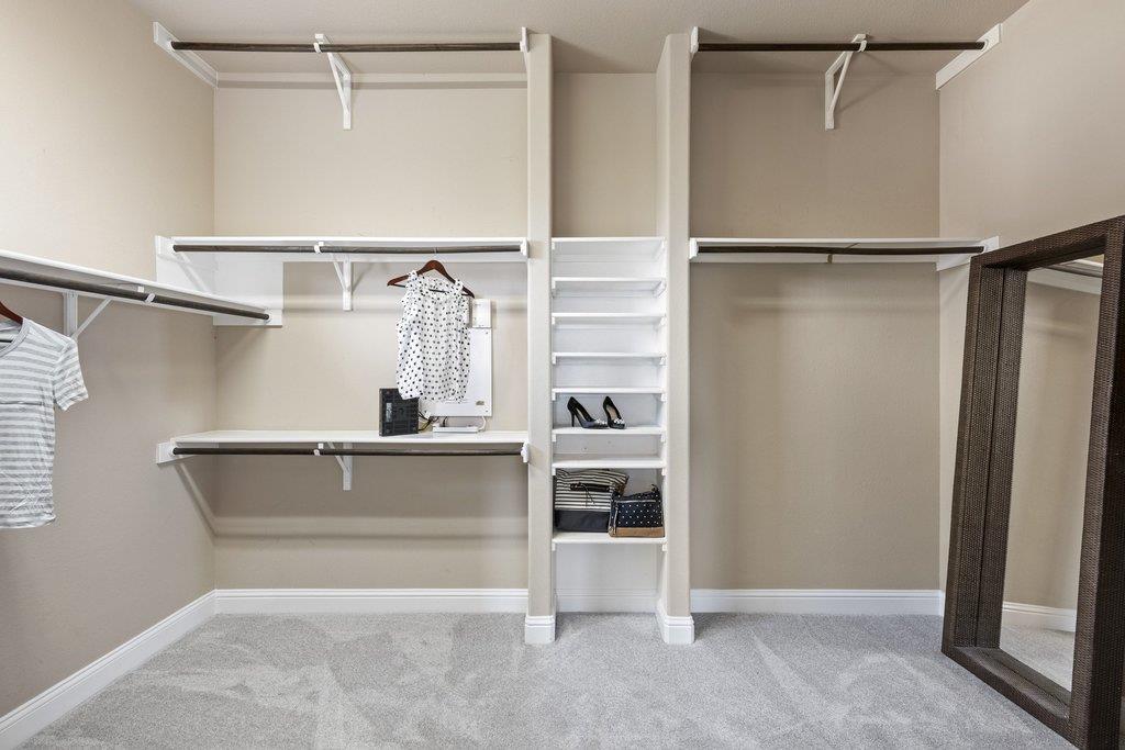 Walk-in closet with built-in shelving, hanging clothes, and a full-length mirror.