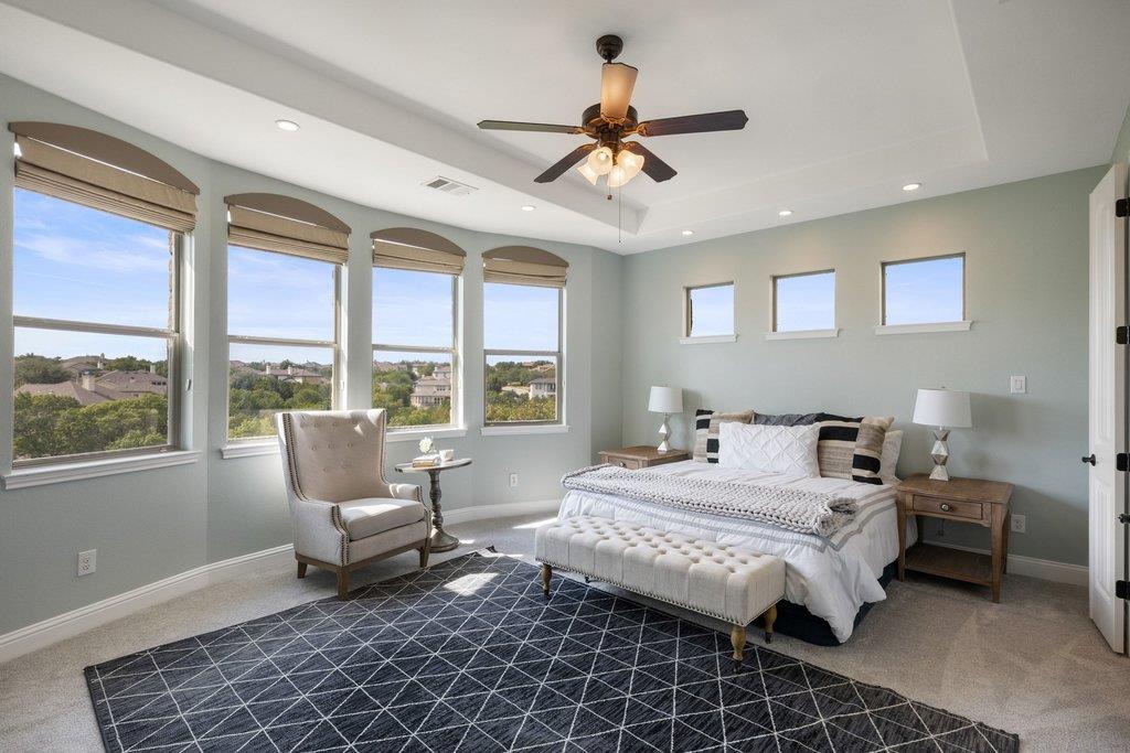 Bedroom with a white bed, dark geometric rug, and tall windows overlooking nearby homes.