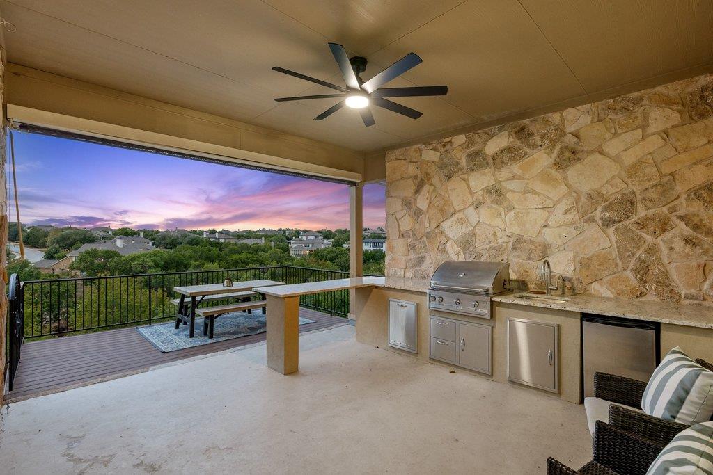 Covered patio with a built-in grill and stone wall overlooking trees at sunset.