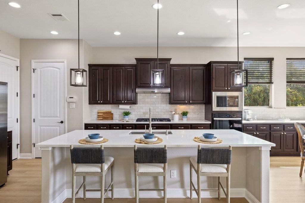 Kitchen with a large white island, dark wood cabinetry, and stainless steel appliances.