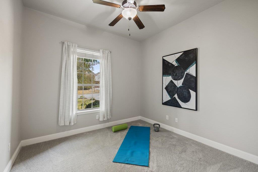 Carpeted exercise room with a blue yoga mat, fitness weights, and a curtained window.