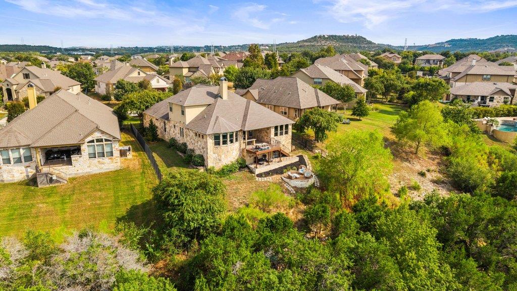 Aerial view of a stone home with a backyard patio, trees, and distant hills.