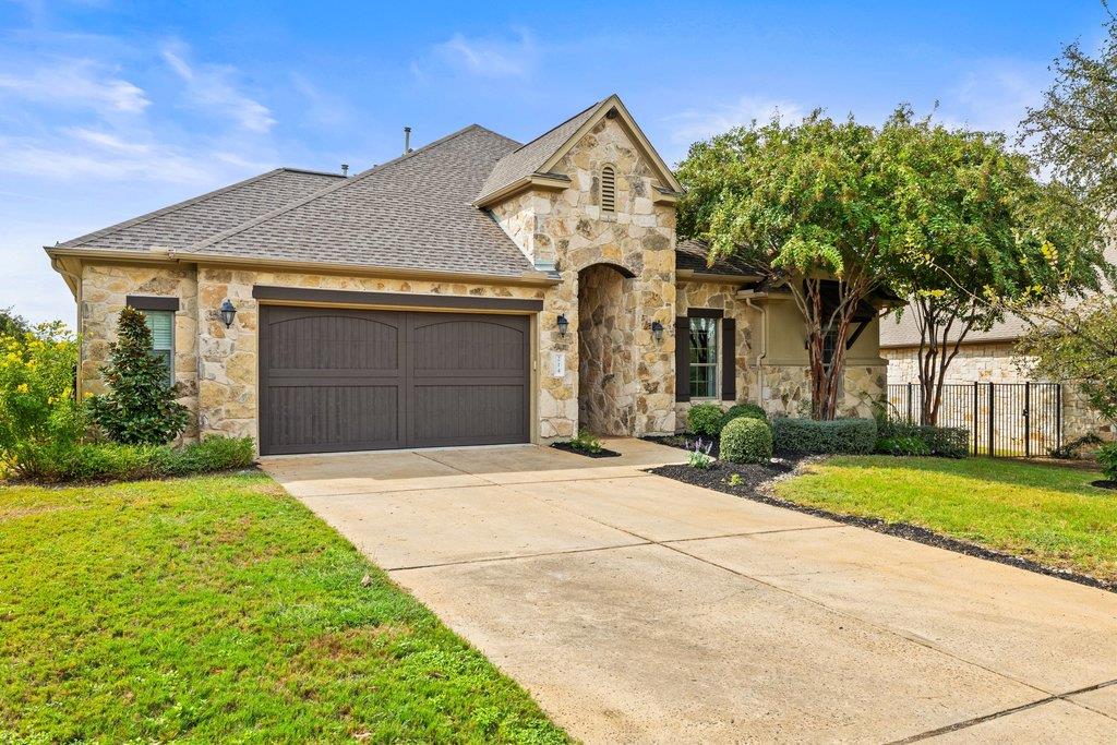 Stone-front house with a double garage, wide driveway, and mature tree in the front yard.
