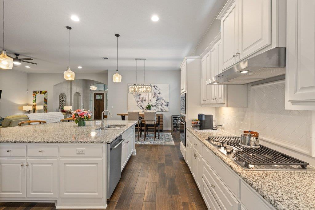 White kitchen with granite island and gas cooktop opening to dining and living areas.