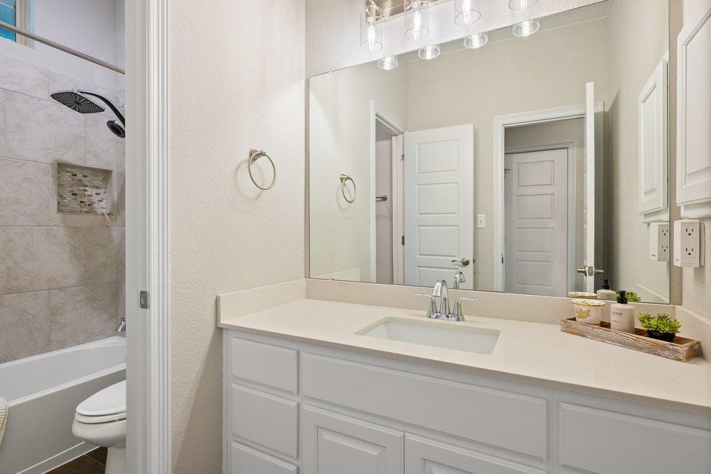 Bathroom with a white vanity and large mirror beside a tiled tub and rainfall shower.