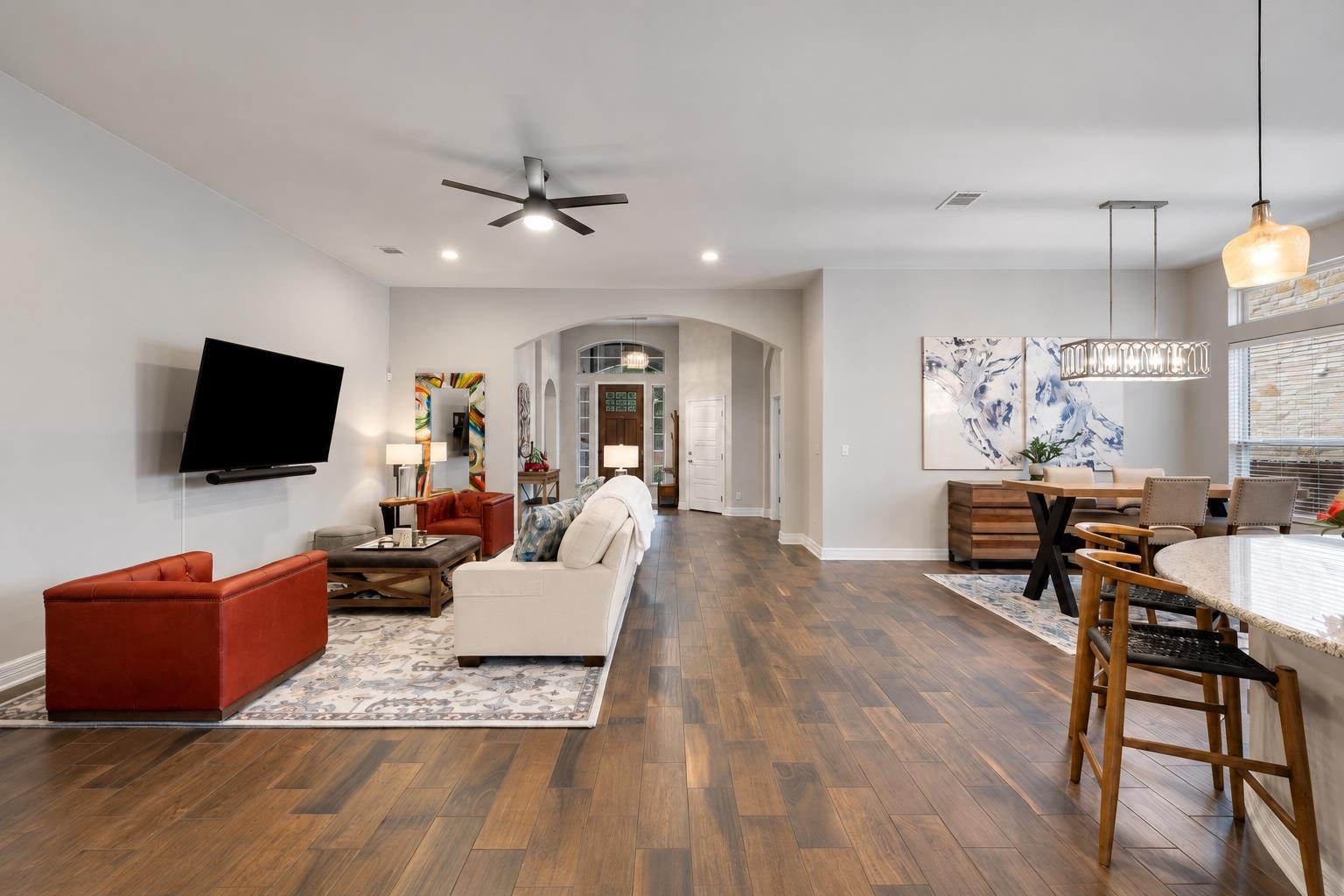 Open living and dining room with wood-look floors, red leather chair, white sofa, and large windows.