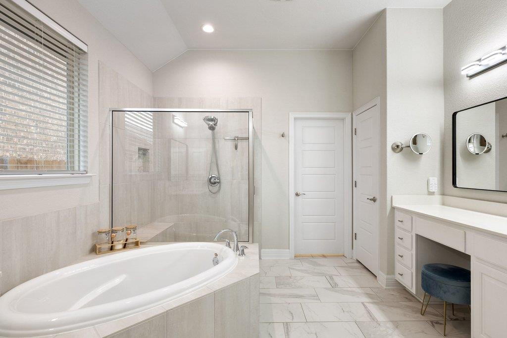 Primary bathroom with a large soaking tub, glass-enclosed shower, and marble-look tile.