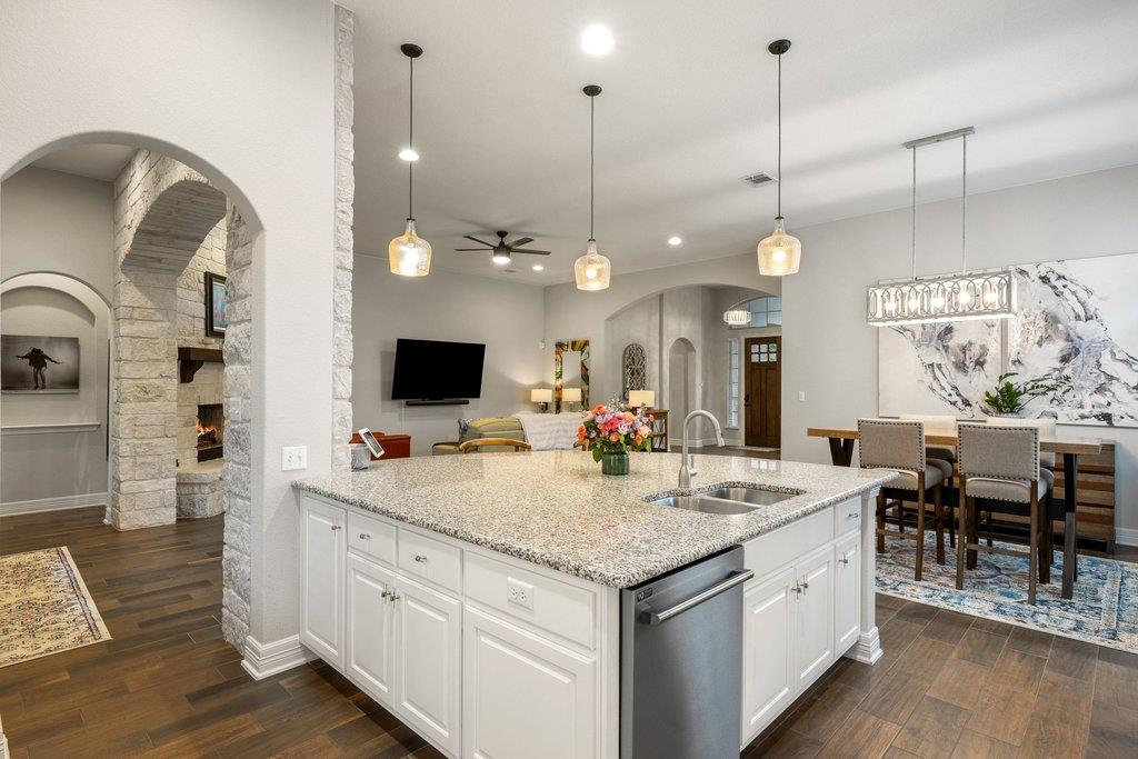 Open-plan kitchen with a large granite island, pendant lights, and dining area beside a stone fireplace.