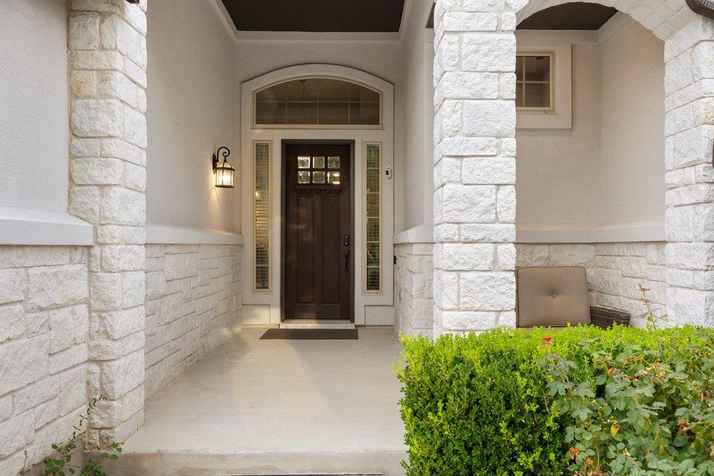Covered front entry with white stone columns, a dark wood door, and trimmed shrubs.