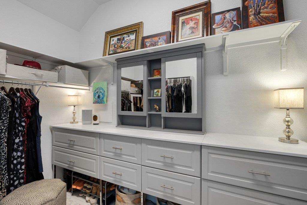 Walk-in closet with gray built-in drawers, hanging clothes, and framed artwork displayed above.