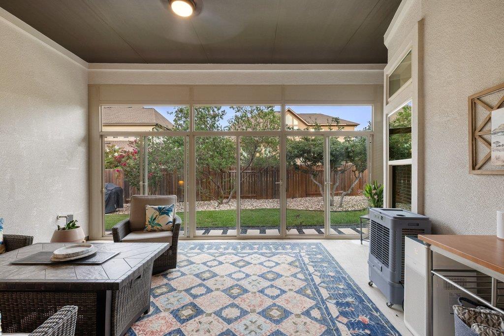 Furnished sunroom with large windows overlooking a fenced backyard and a blue patterned rug.