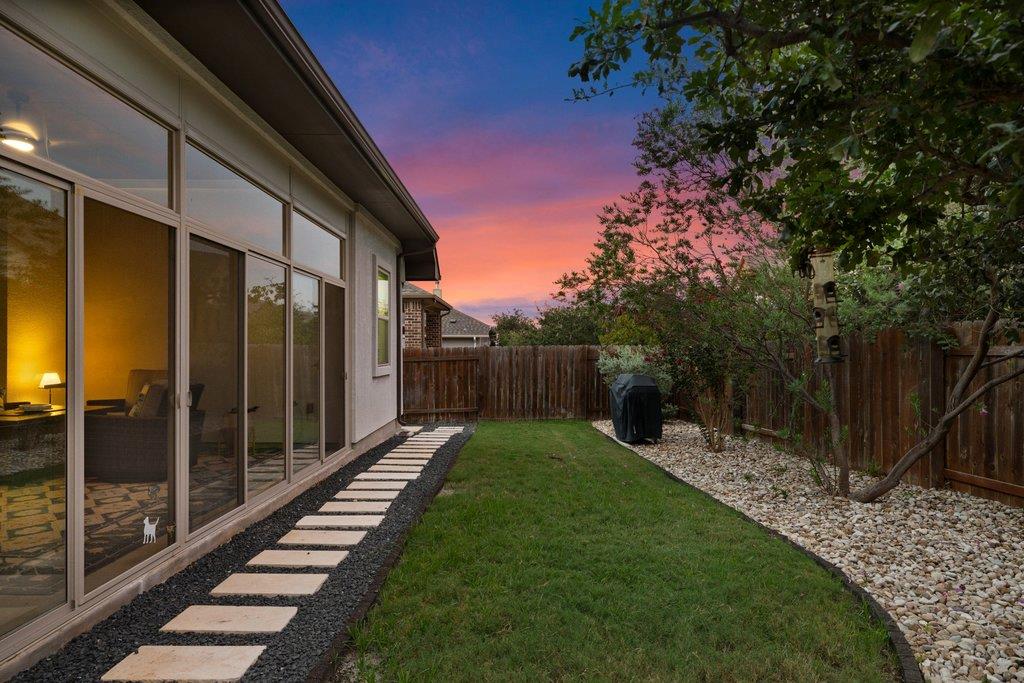 Backyard at dusk with a curved lawn, stepping-stone path, and large glass doors.