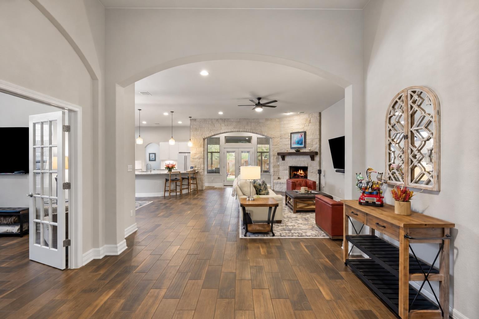 Open-plan living room with wood-look floors, stone fireplace wall, and kitchen island.
