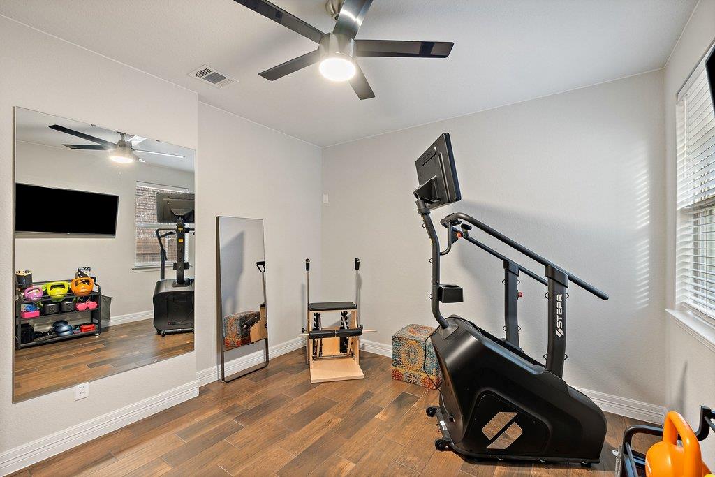 Home gym with a large wall mirror, stationary exercise bike, free weights, and wood-look flooring.