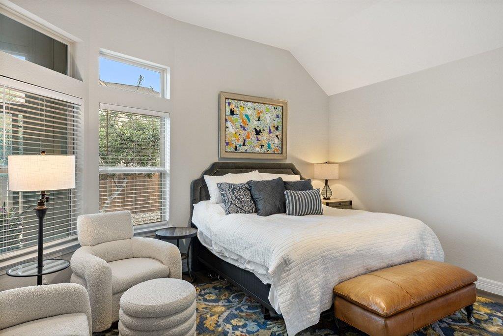 Bedroom with a king-size bed, tall windows, upholstered chairs, and colorful artwork.