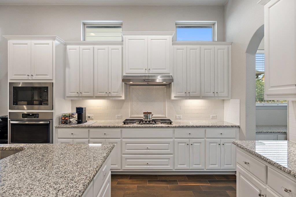 Bright kitchen with white cabinetry, granite counters, a central gas cooktop, and dark wood flooring.