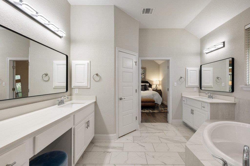 Primary bathroom with a long double vanity, marble-look floors, and a built-in soaking tub.