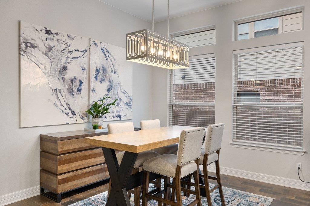 Dining room with a wood table, upholstered chairs, geometric pendant light, and tall windows.