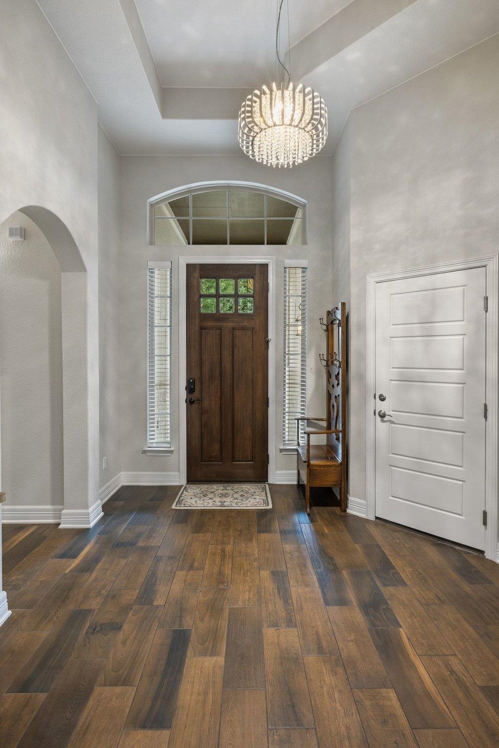 Entry foyer with a dark wood front door, arched transom window, and crystal chandelier.