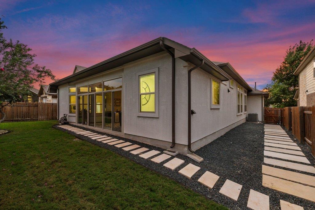 Modern gray home’s rear exterior with large glass doors and stepping-stone paths at dusk.