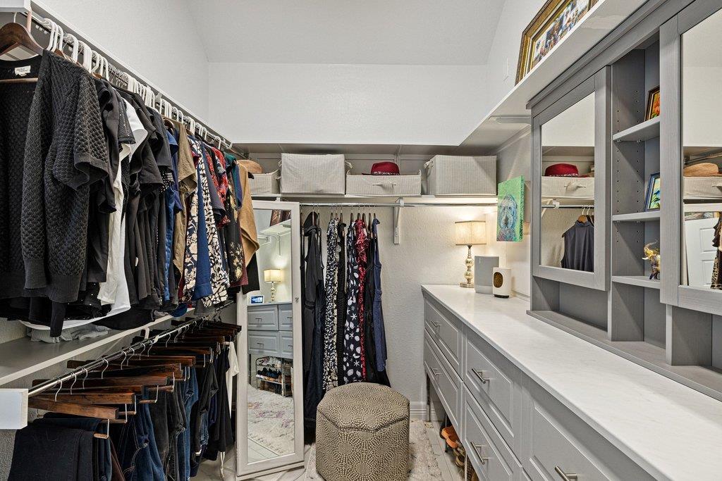 Walk-in closet with clothing rails, a full-length mirror, and a long built-in dresser with countertop.