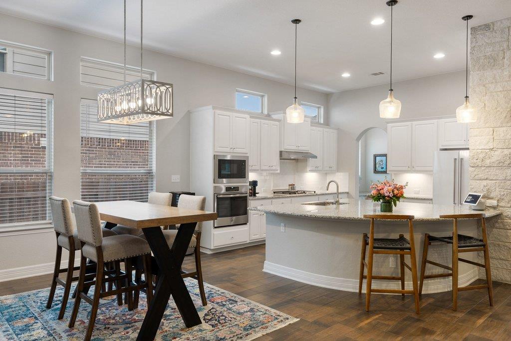 Open-plan kitchen with a granite island and bar stools beside a dining table and tall windows.