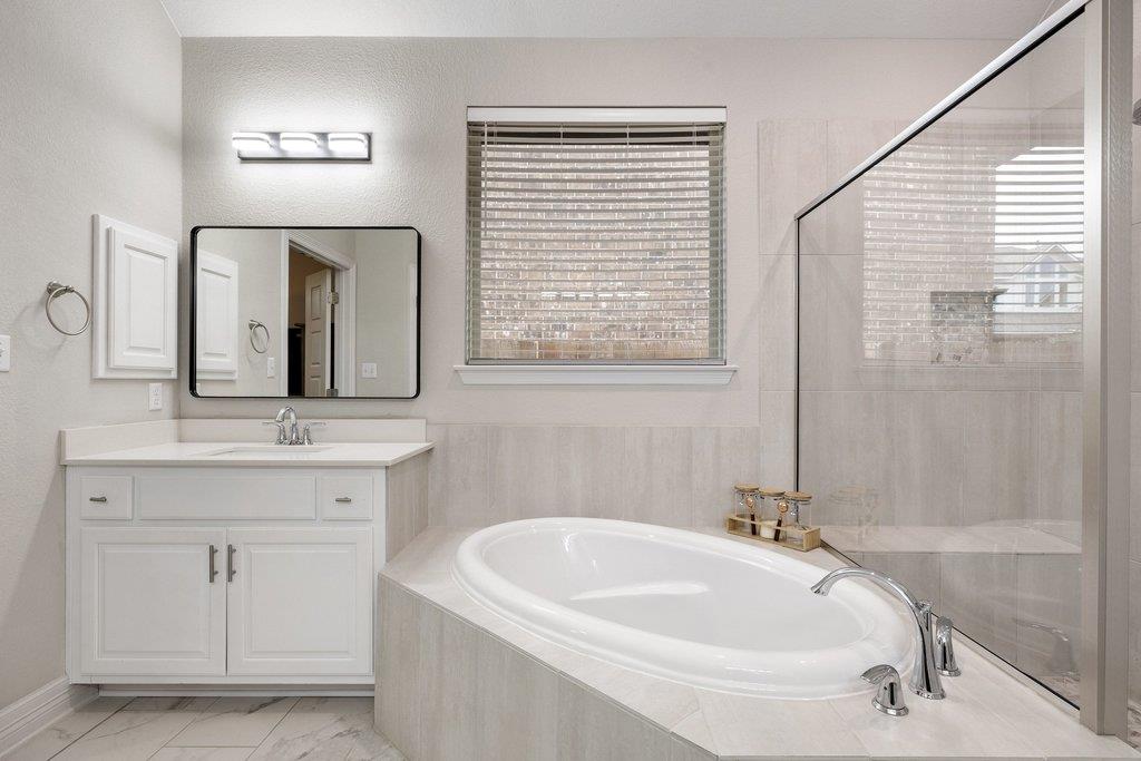 Bathroom with a built-in soaking tub, white vanity, and glass-enclosed shower.