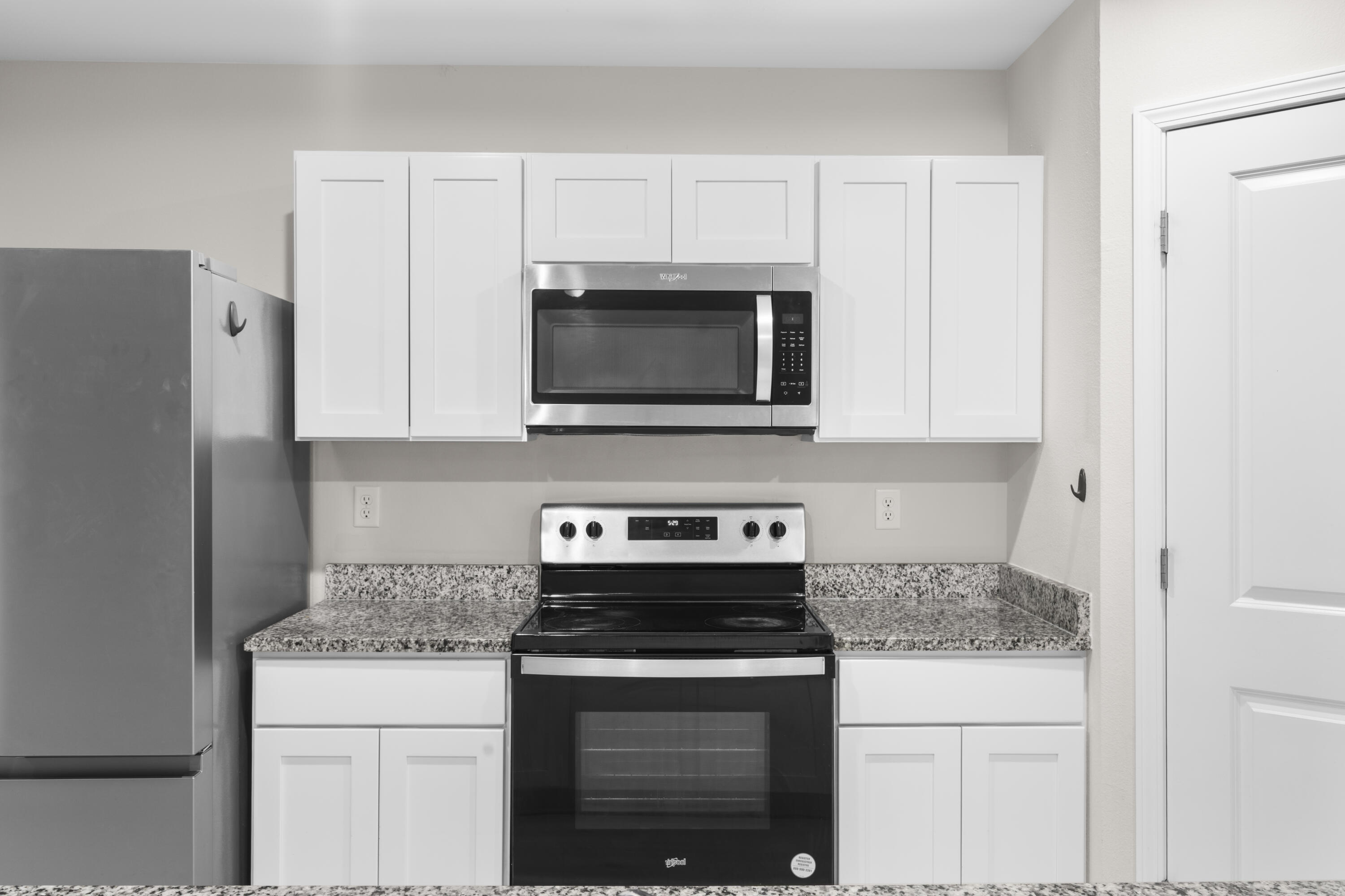Kitchen with white cabinets, granite counters, stainless refrigerator, and electric range.
