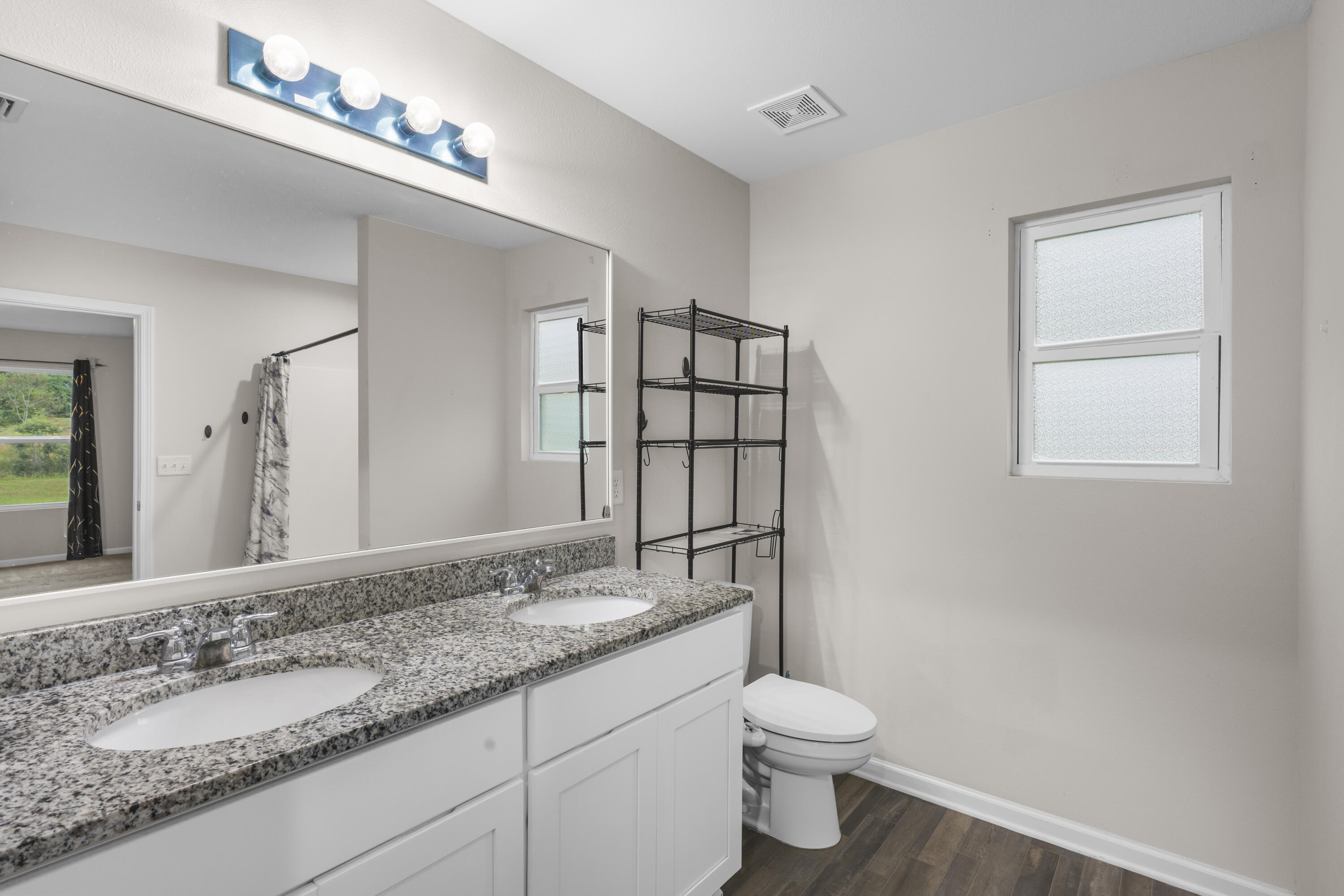 Bathroom with double-sink granite vanity, large mirror, and frosted windows.