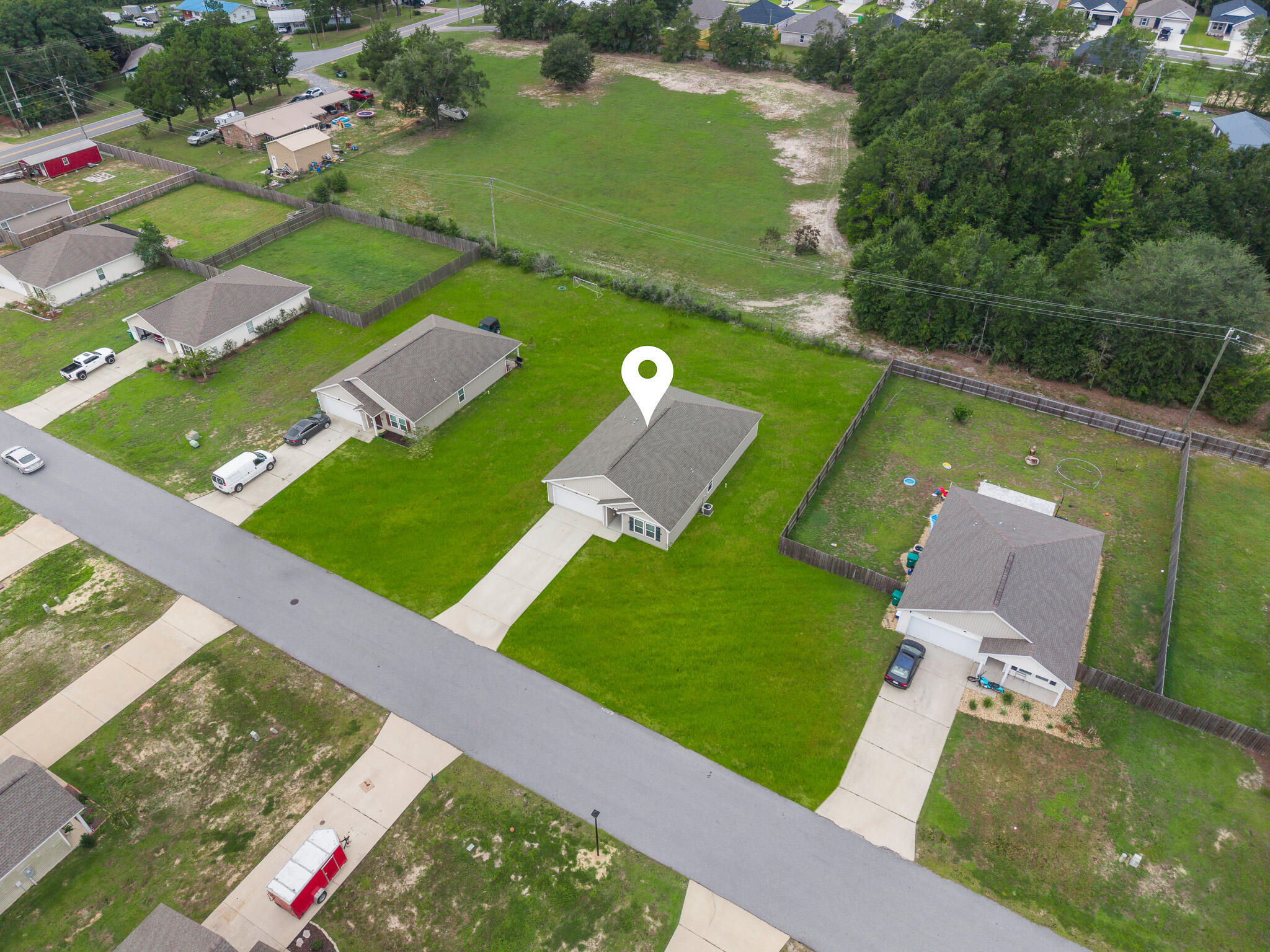 Aerial view of a single-story home with a location pin, green lawn, and neighboring houses.